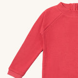 A close up of the Little Green Radicals pink berry waffle long sleeve cosy top showing the waffle and popper fastener detail on pink organic cotton fabric