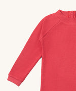 A close up of the Little Green Radicals pink berry waffle long sleeve cosy top showing the waffle and popper fastener detail on pink organic cotton fabric
