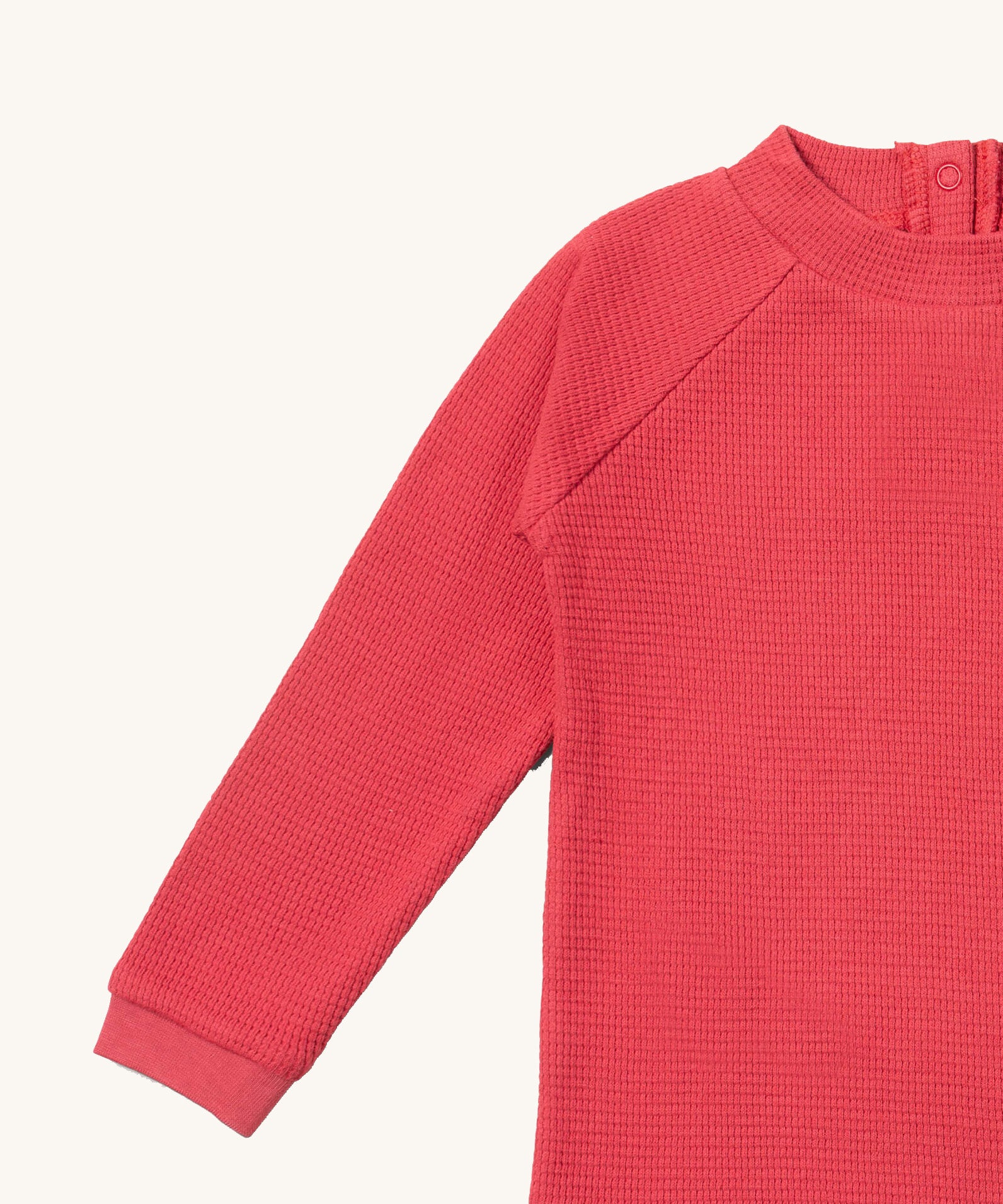 A close up of the Little Green Radicals pink berry waffle long sleeve cosy top showing the waffle and popper fastener detail on pink organic cotton fabric