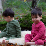2 children wearing the holly berry pink and green chive waffle playsuit. A long sleeves all in one suit made from GOTs organic cotton fabric with button fasteners and a small pouch chest pocket