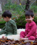 2 children wearing the holly berry pink and green chive waffle playsuit. A long sleeves all in one suit made from GOTs organic cotton fabric with button fasteners and a small pouch chest pocket