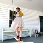 Girl stood swinging on the Lillagunga grand oak swing on a white wooden porch