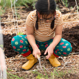Child wearing the Little Green Radicals apple picking green comfy organic cotton joggers with a short sleeved gold and cream striped t-shirt and yellow wellington boots. 