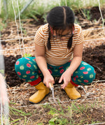 Child wearing the Little Green Radicals apple picking green comfy organic cotton joggers with a short sleeved gold and cream striped t-shirt and yellow wellington boots. 