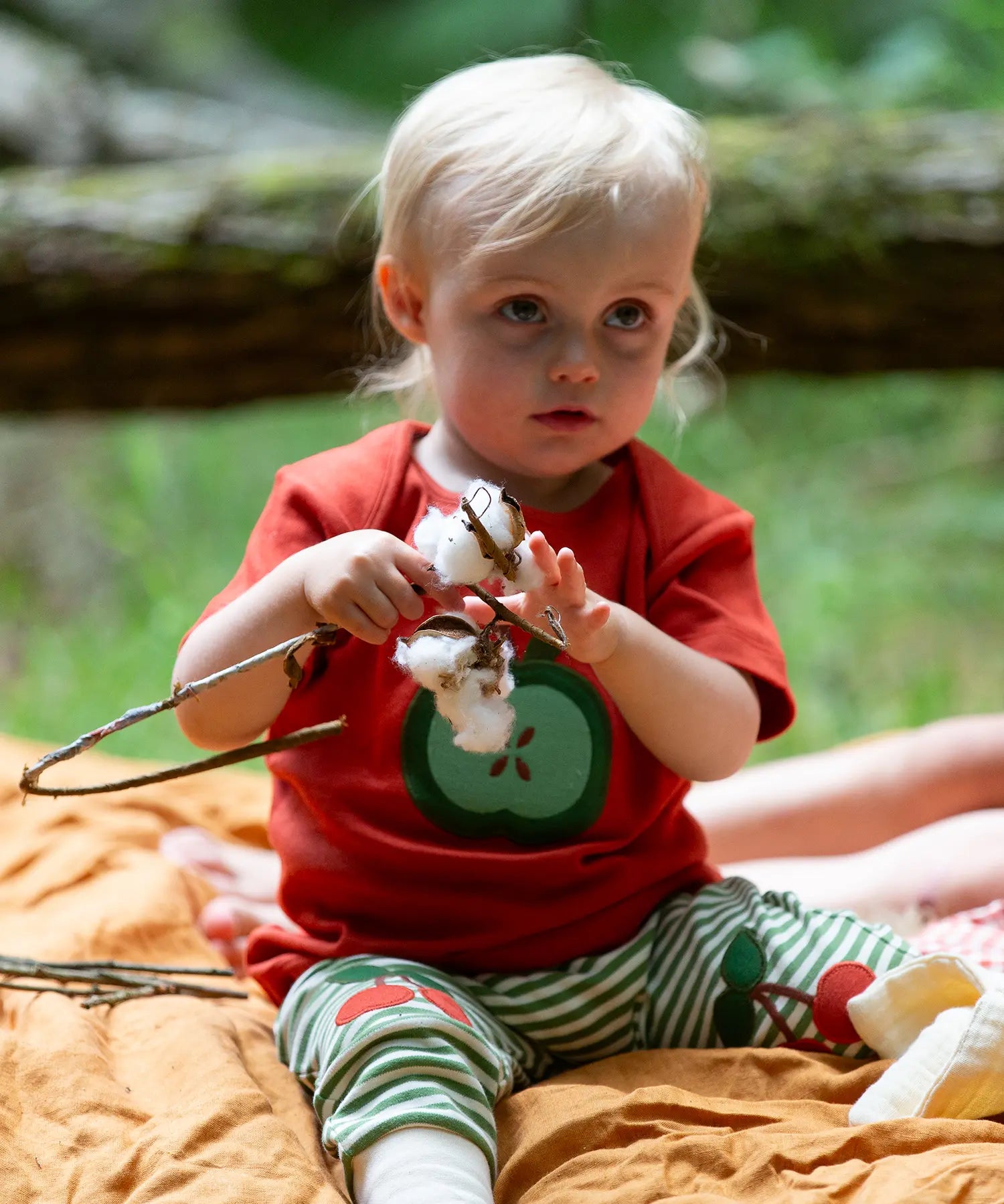 Child wearing the Little Green Radicals green apple applique organic short sleeve red t-shirt with cherry knee patch joggers.