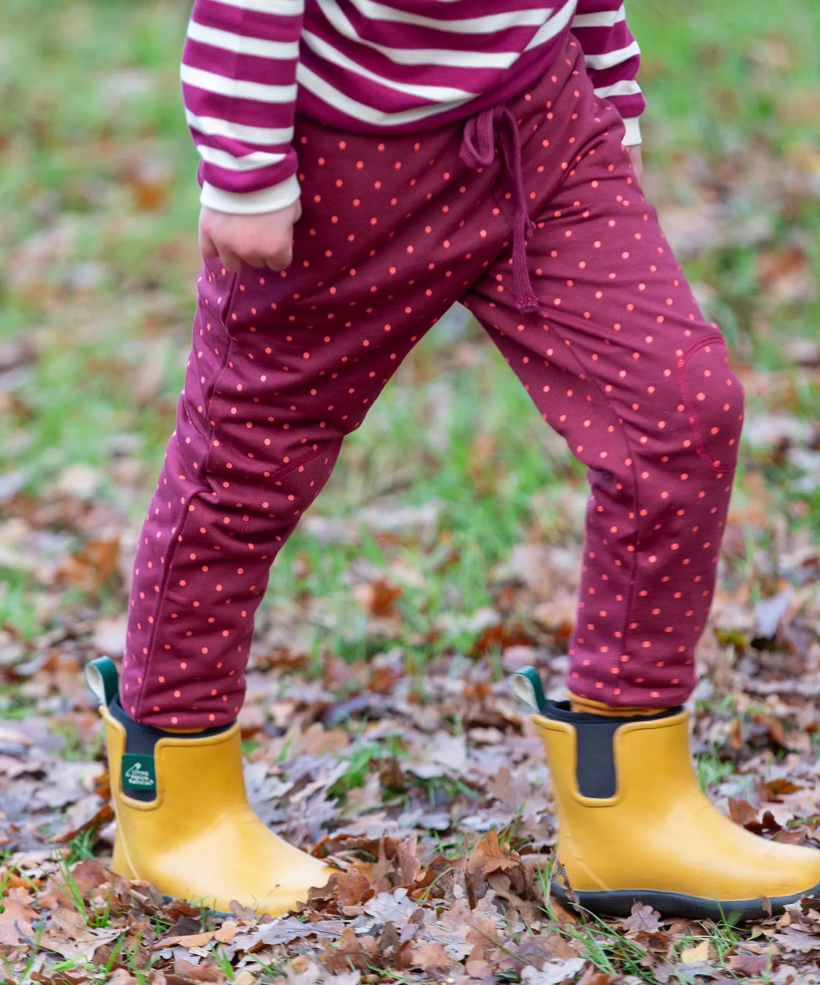 Close up of child wearing the Little Green Radicals autumn polkadot cosy cotton knee patch joggers with yellow gold wellington boots.