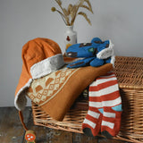 Little Green Radicals gold yellow mountain fair isle snuggly woollen jumper placed on wicker basket with a corduroy flapper hat, bear sherpa gloves and striped socks. 