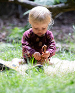 A young child sitting on grass wearing a Little Green Radicals Baby Bodysuit 2 Pack featuring a Brown Bears print. Little Green Radicals offer a range of organic cotton children's clothing available here at Babipur. 