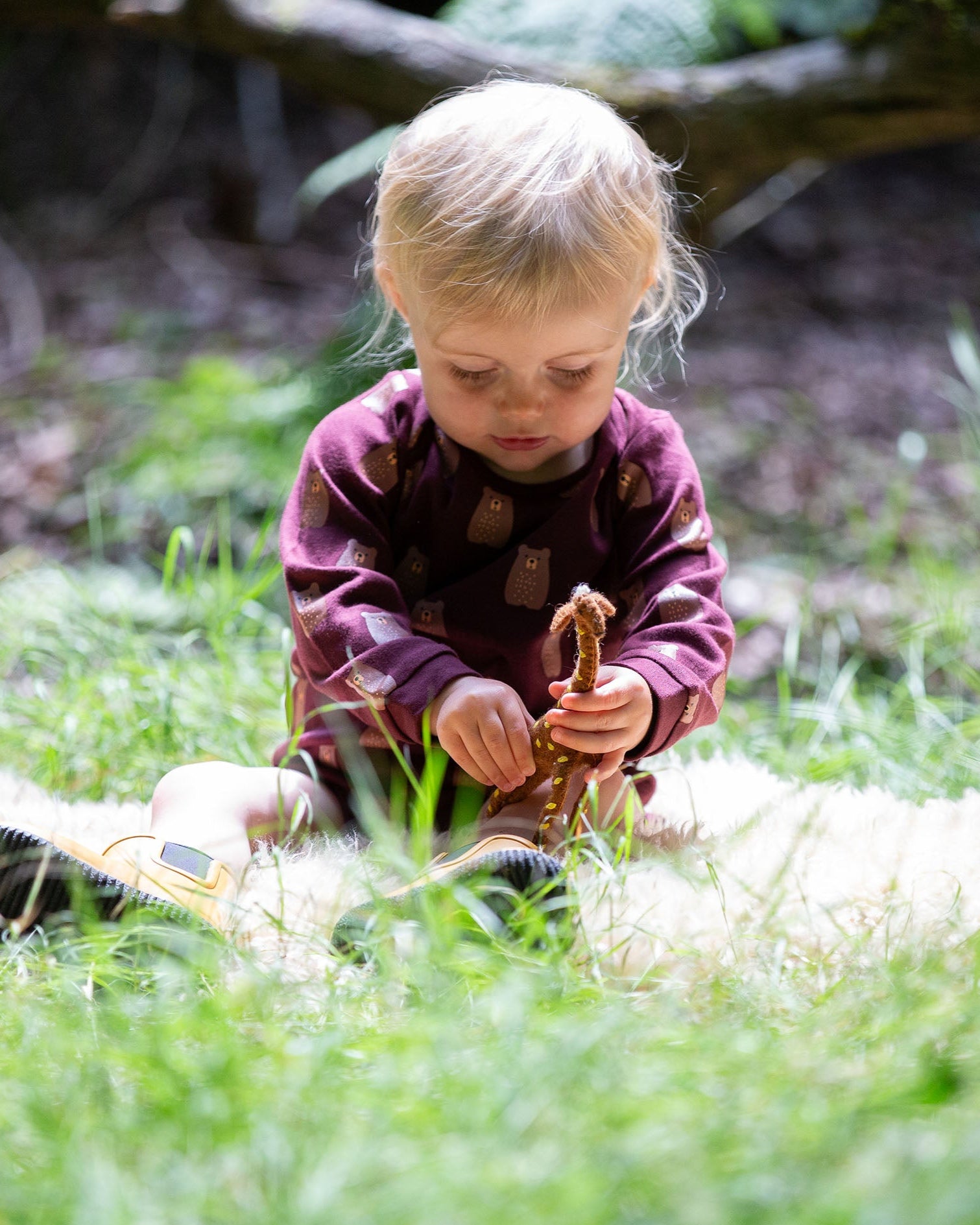 A young child sitting on grass wearing a Little Green Radicals Baby Bodysuit 2 Pack featuring a Brown Bears print. Little Green Radicals offer a range of organic cotton children's clothing available here at Babipur. 