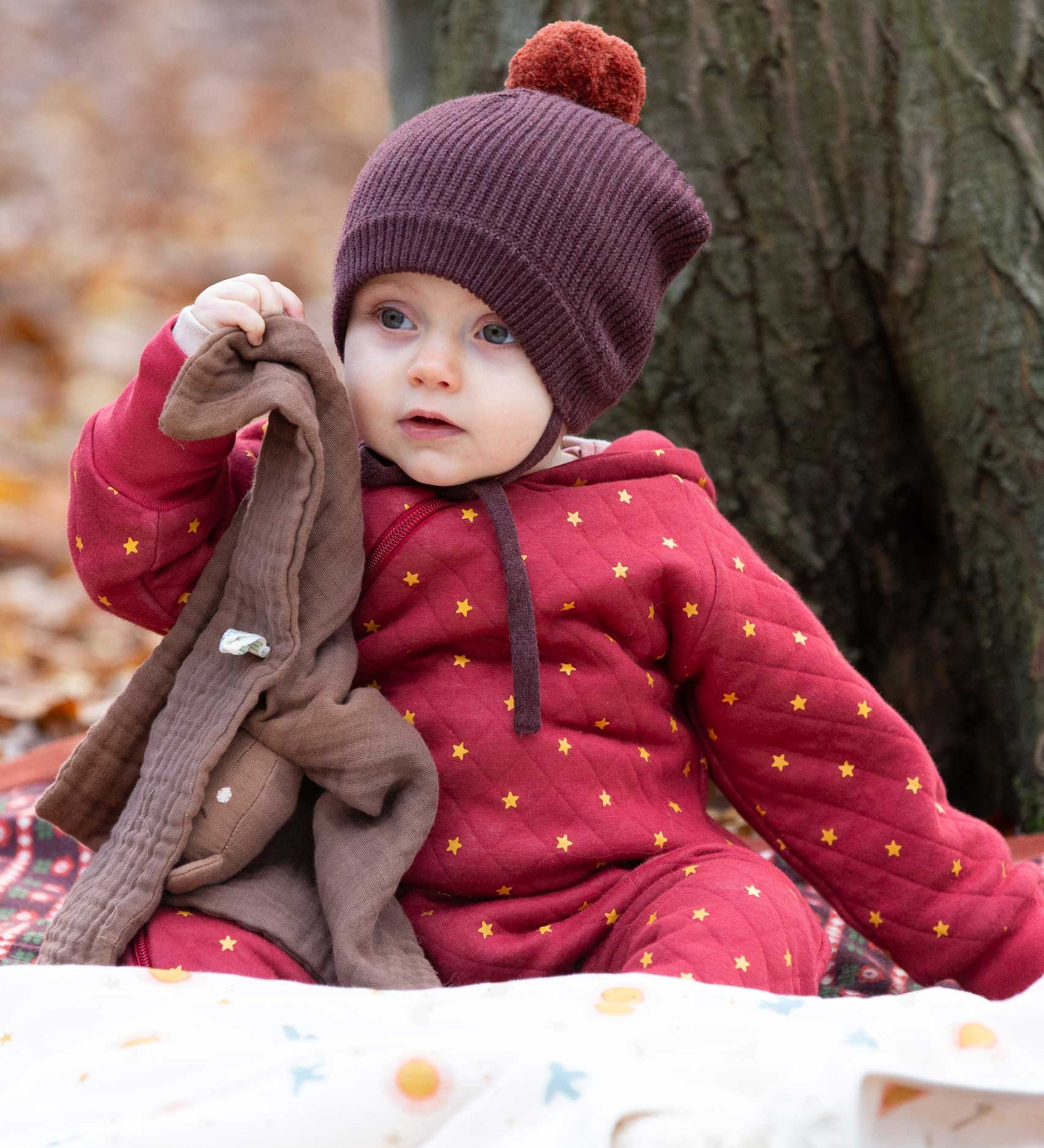 A baby wearing the Little Green Radicals Organic Cotton Quilted Snug Suit with a Red Stars design. This snug suit is a part of a wide range of organic cotton clothing for children available here at Babipur. 