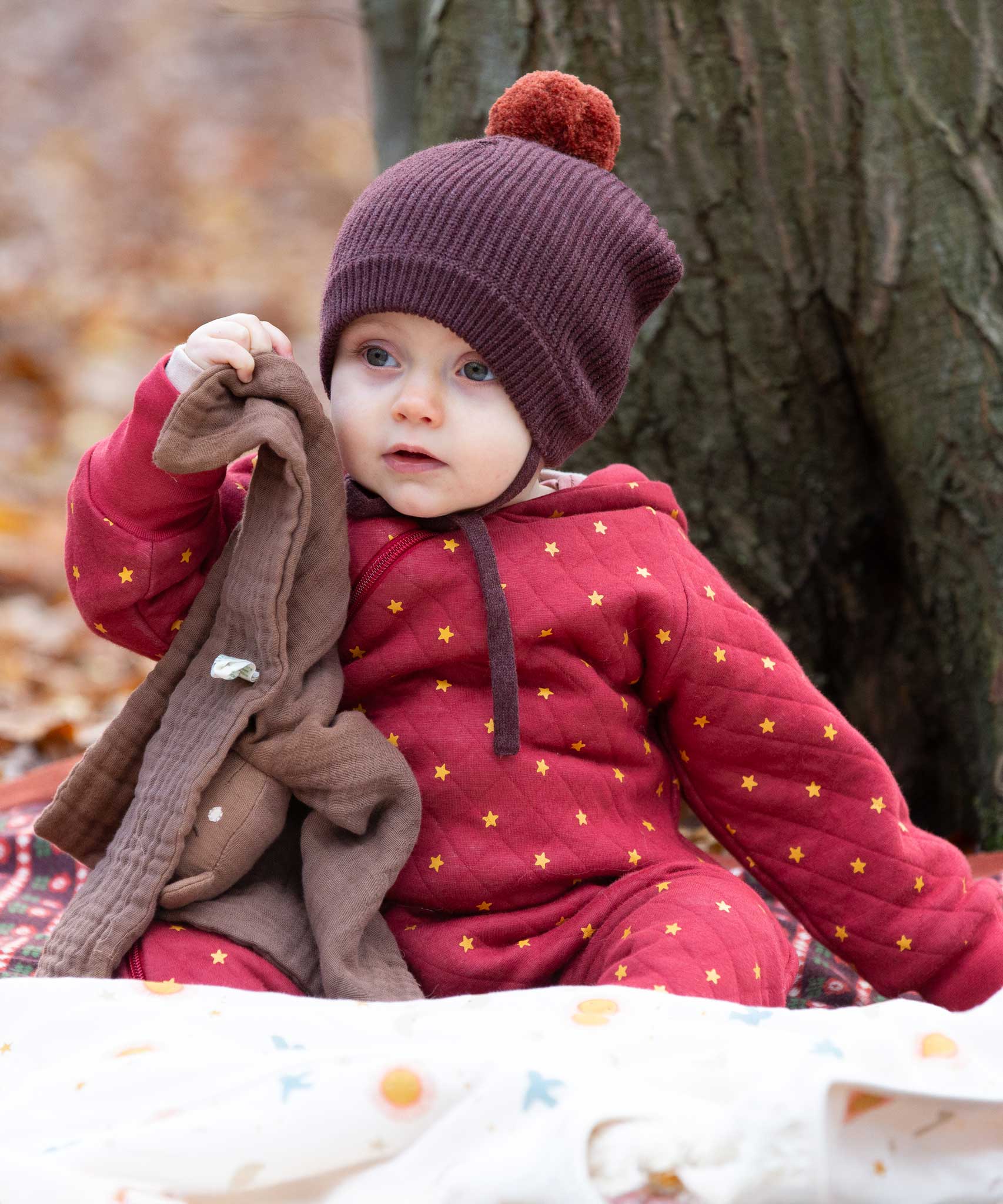 A baby wearing the Little Green Radicals Organic Cotton Quilted Snug Suit with a Red Stars design. This snug suit is a part of a wide range of organic cotton clothing for children available here at Babipur. 
