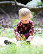 A young child sitting on grass wearing a Little Green Radicals Baby Bodysuit 2 Pack featuring a Brown Bears print. Little Green Radicals offer a range of organic cotton children's clothing available here at Babipur. 