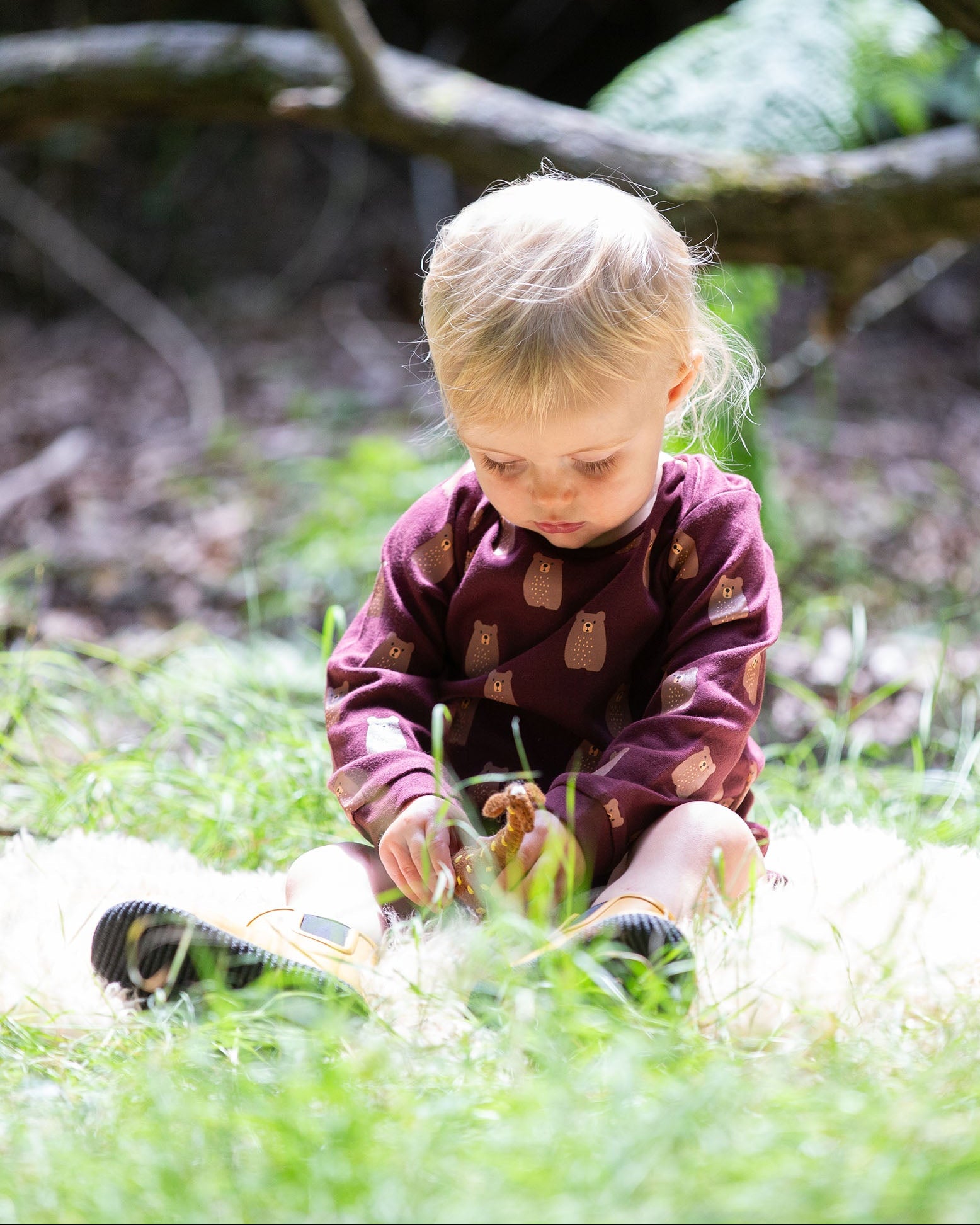 A young child sitting on grass wearing a Little Green Radicals Baby Bodysuit 2 Pack featuring a Brown Bears print. Little Green Radicals offer a range of organic cotton children's clothing available here at Babipur. 