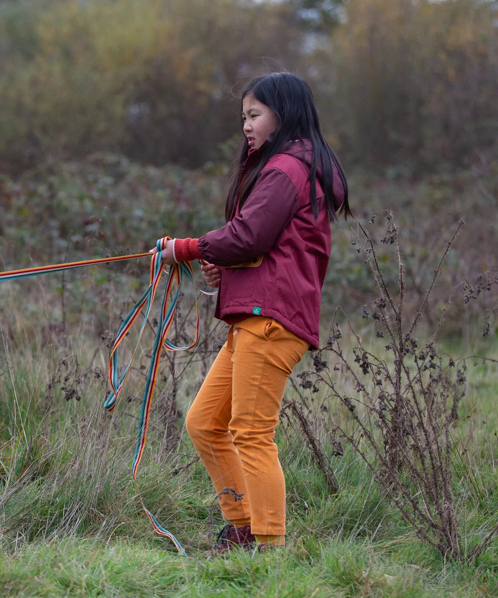 Child wearing a Little Green Radicals  berry purple recycled waterproof winter coat with yellow gold trousers.
