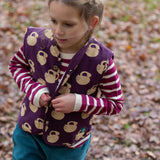 Child wearing the Little Green Radicals berry purple striped long sleeve top with green joggers and a purple sleeping swan gilet.