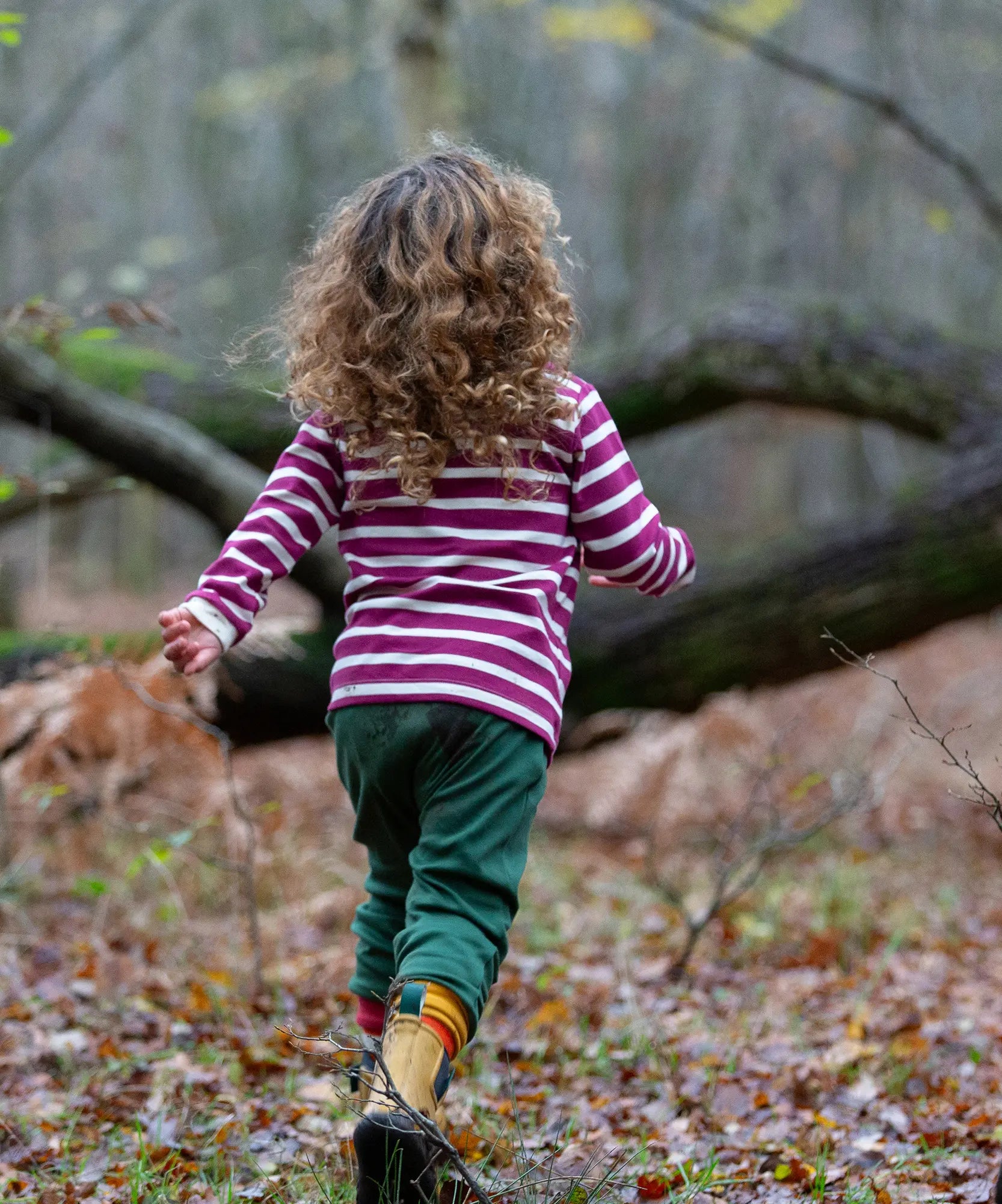 Child wearing the Little Green Radicals berry purple striped long sleeve top with green joggers.