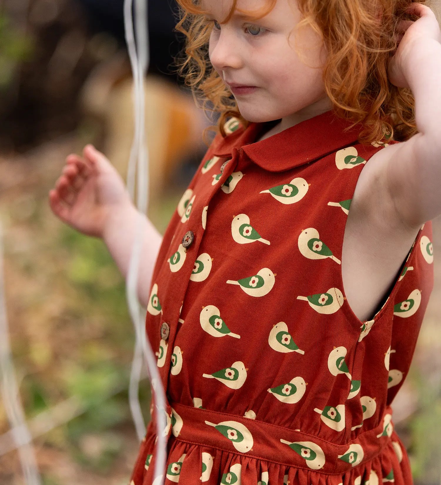 Close up of button up front on the Little Green Radicals child's red repeated spring birds print collared pinafore dress worn by a child. 