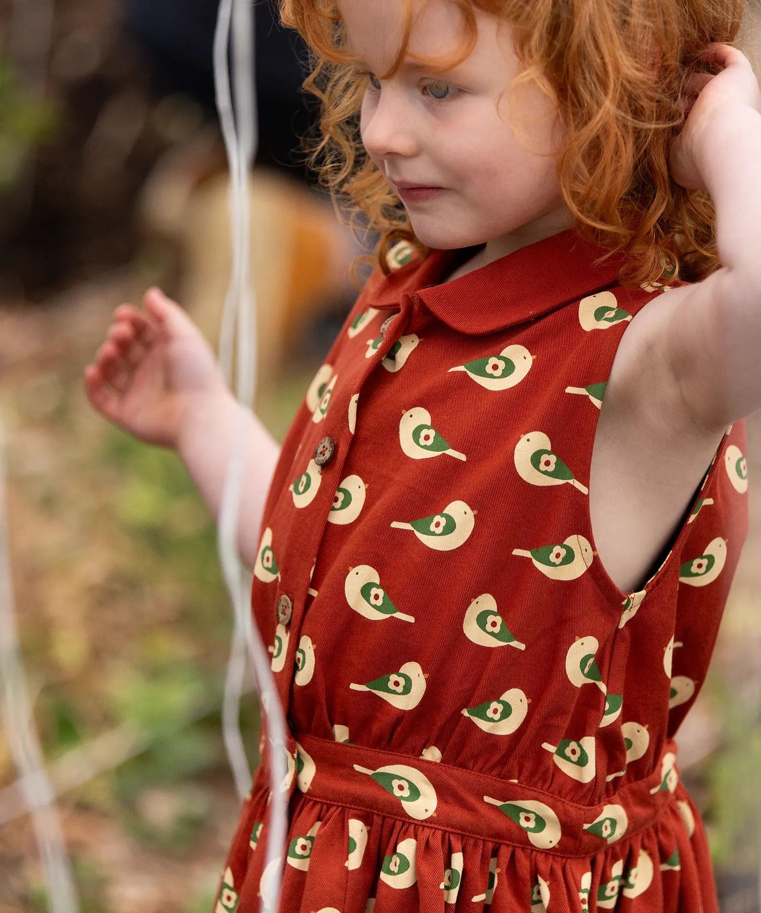 Close up of button up front on the Little Green Radicals child's red repeated spring birds print collared pinafore dress worn by a child. 
