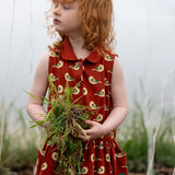 Child wearing the Little Green Radicals child's red repeated spring birds print collared pinafore button dress. 