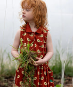 Child wearing the Little Green Radicals child's red repeated spring birds print collared pinafore button dress. 