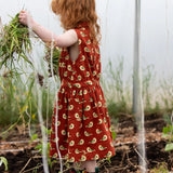Child wearing the Little Green Radicals child's red repeated spring birds print collared pinafore button dress with red wellington boots.