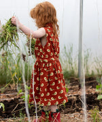 Child wearing the Little Green Radicals child's red repeated spring birds print collared pinafore button dress with red wellington boots.
