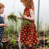 Child wearing the Little Green Radicals child's red repeated spring birds print collared pinafore button dress. 