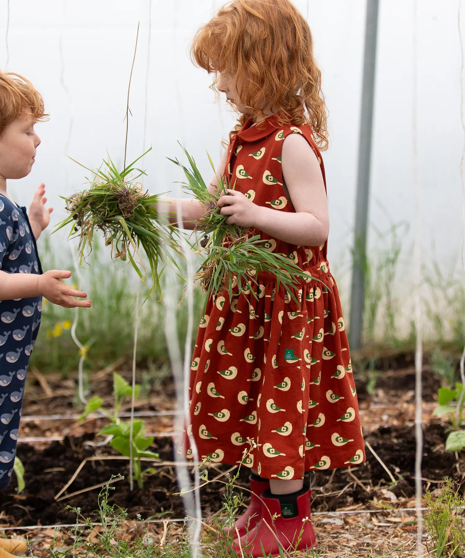 Child wearing the Little Green Radicals child's red repeated spring birds print collared pinafore button dress. 