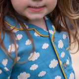 A close up of the front of the top from the Little Green Radicals Blue Clouds Button Through Pyjama Short Set. The set contains a traditional style, short sleeved shirt style top with matching shorts. The print has a blue background with an over white cloud print. Little green Radicals have a wide range of organic cotton, Fairtrade children's clothing and outerwear available here at Babipur.