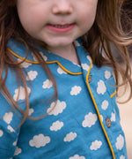 A close up of the front of the top from the Little Green Radicals Blue Clouds Button Through Pyjama Short Set. The set contains a traditional style, short sleeved shirt style top with matching shorts. The print has a blue background with an over white cloud print. Little green Radicals have a wide range of organic cotton, Fairtrade children's clothing and outerwear available here at Babipur.