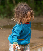 A child wearing the Little Green Radicals From One To Another Deep Blue Colour Block Knitted Cardigan. This organic cotton cardigan is part of a wide range of organic cotton, Fairtrade children's clothing and outerwear available here at Babipur.
