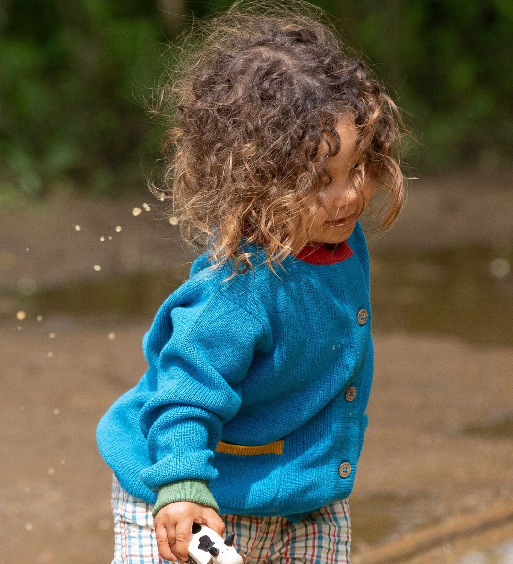 A child wearing the Little Green Radicals From One To Another Deep Blue Colour Block Knitted Cardigan. This organic cotton cardigan is part of a wide range of organic cotton, Fairtrade children's clothing and outerwear available here at Babipur.