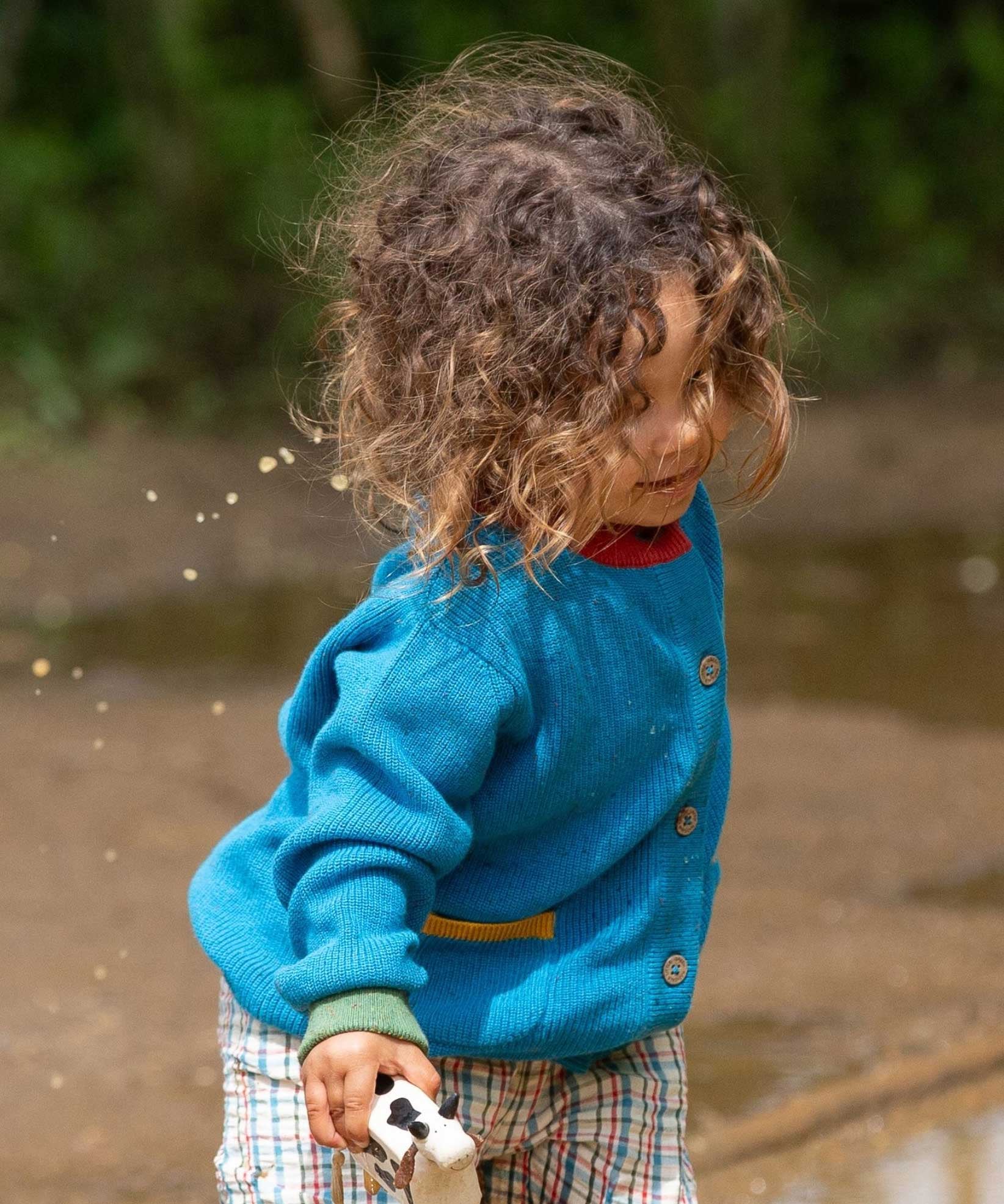 A child wearing the Little Green Radicals From One To Another Deep Blue Colour Block Knitted Cardigan. This organic cotton cardigan is part of a wide range of organic cotton, Fairtrade children's clothing and outerwear available here at Babipur.