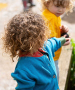 A child wearing the Little Green Radicals From One To Another Deep Blue Colour Block Knitted Cardigan. This organic cotton cardigan is part of a wide range of organic cotton, Fairtrade children's clothing and outerwear available here at Babipur.