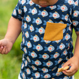 A close up of the short sleeved top from the Little Green Radicals little fish organic cotton t-shirt and jogger playset outfit. A navy top with repeat fish print and a yellow chest pocket with blue and cream striped joggers.