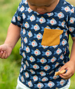 A close up of the short sleeved top from the Little Green Radicals little fish organic cotton t-shirt and jogger playset outfit. A navy top with repeat fish print and a yellow chest pocket with blue and cream striped joggers.