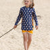 Child on beach wearing the Little Green Radicals little fish print blue UPF 50 sunsafe long sleeve rash vest with yellow side panels and matching yellow gold swim shorts.
