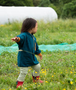 Child wearing a Little Green Radicals children's atlantic deep blue organic cotton quarter zip hoodie with striped leggings underneath and red wellington boots. 