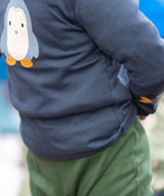 Close up of a child wearing the Little Green Radicals blue penguins applique long sleeve organic cotton top in navy.