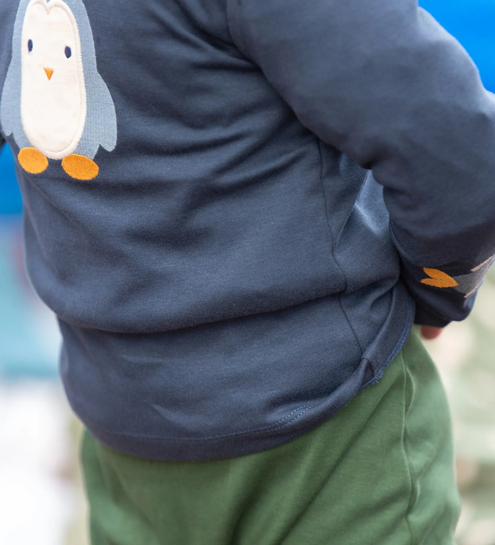 Close up of a child wearing the Little Green Radicals blue penguins applique long sleeve organic cotton top in navy.
