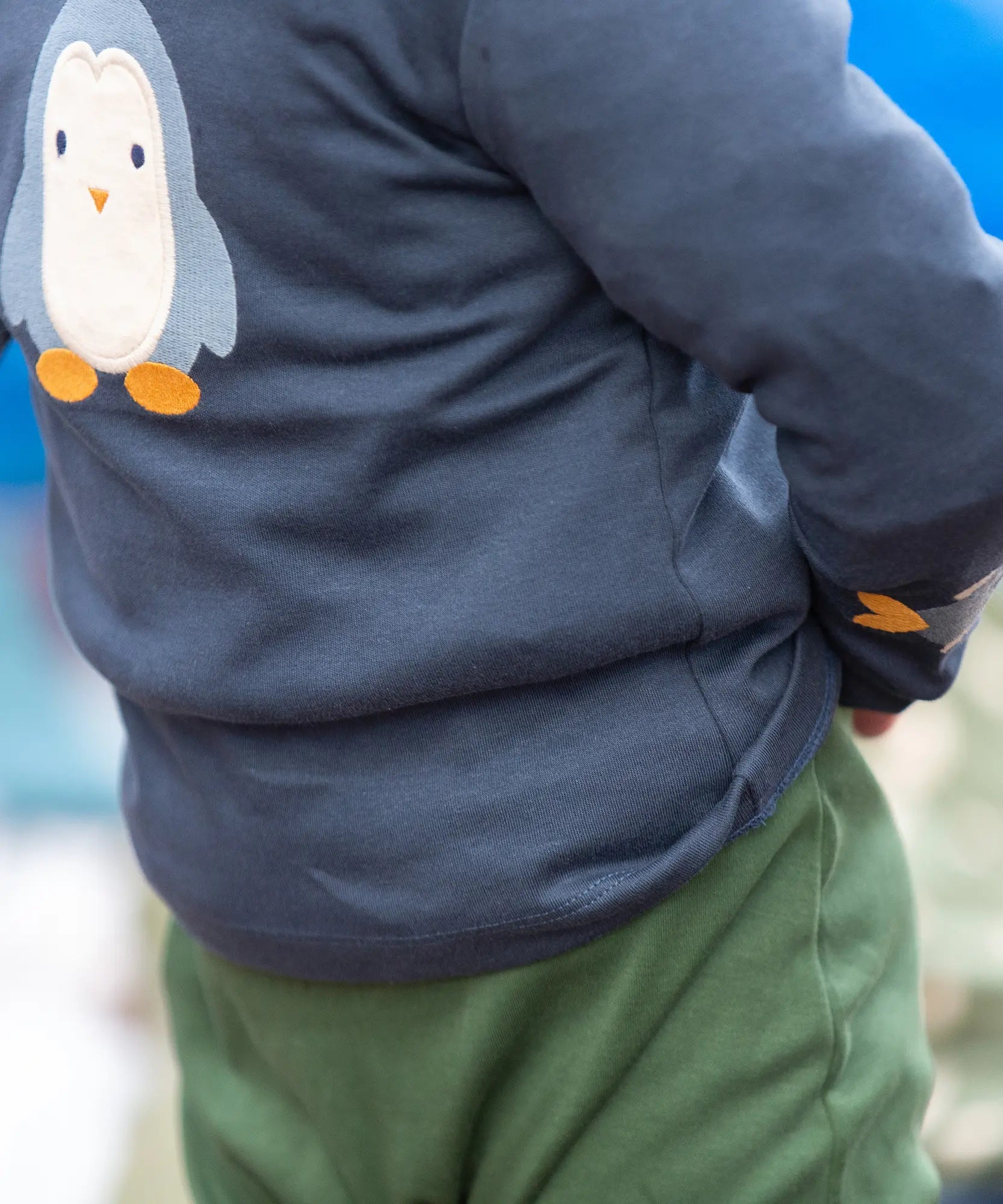 Close up of a child wearing the Little Green Radicals blue penguins applique long sleeve organic cotton top in navy.