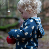 Child wearing a Little Green Radicals navy blue penguins hooded reversible snug suit. One side has a penguin print, the other is striped. 
