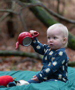 Baby wearing the Little Green Radicals blue penguins GOTS organic cotton zip up babygrow sitting on a green blanket outdoors. Navy blue coloured cotton with an all over penguin print.