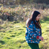 Child wearing a Little Green Radicals blue sun birds recycled waterproof adventure Winter coat with green trousers.