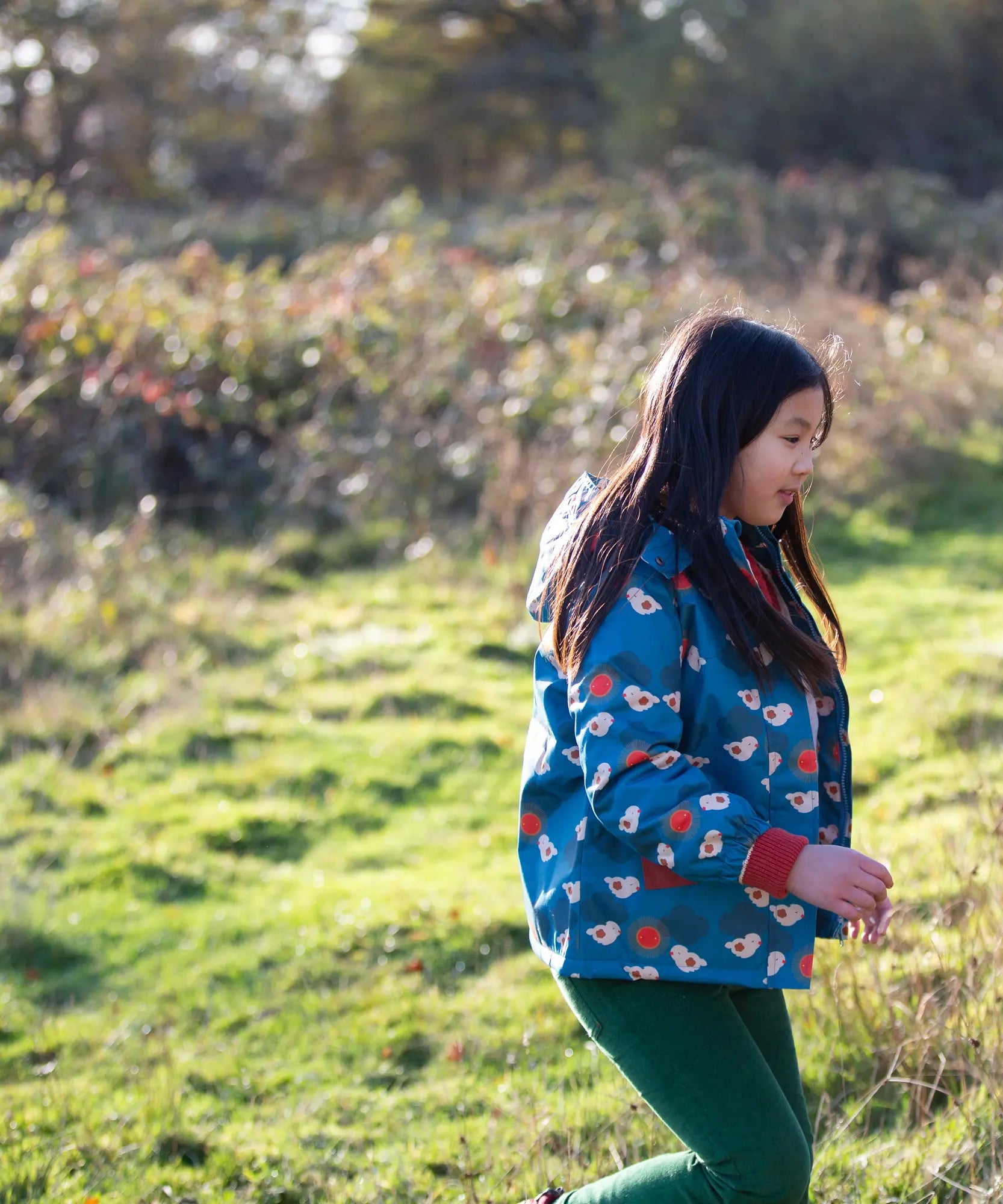 Child wearing a Little Green Radicals blue sun birds recycled waterproof adventure Winter coat with green trousers.