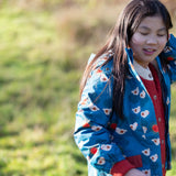 Child wearing a Little Green Radicals blue sun birds recycled waterproof adventure Winter coat with a red knitted cardigan underneath.