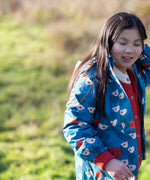Child wearing a Little Green Radicals blue sun birds recycled waterproof adventure Winter coat with a red knitted cardigan underneath.