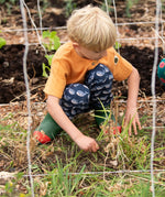 Child wearing the Little Green Radicals navy singing whales print comfy organic cotton joggers with a yellow muslin henley t-shirt and green and red wellingtons.