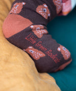 A close up of the Little Green Radicals brown teddy bear organic cotton socks on a child's feet. These socks are part of a wide range of organic cotton clothing and accessories for children available here at Babipur. 