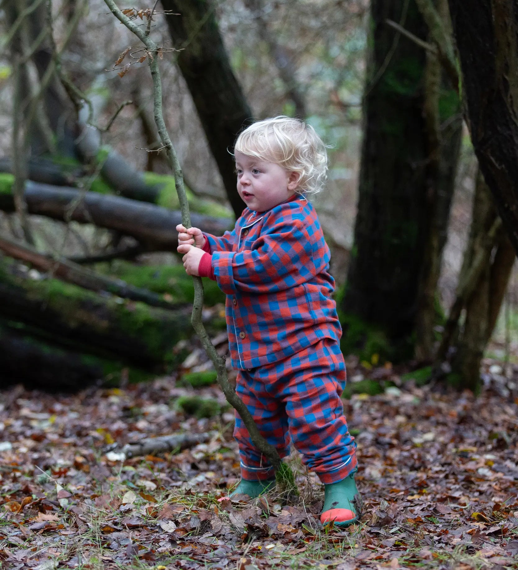Child wearing the Little Green Radicals burnt ochre check classic pyjamas with green wellingtons.